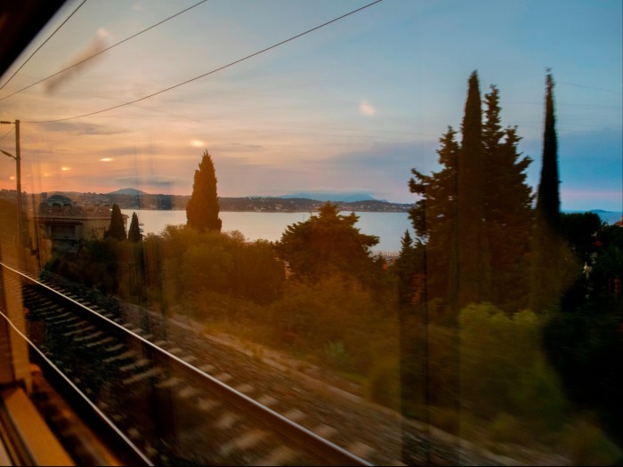 Vedere prin fereastra unui tren a șinelor, a copacilor și, în depărtare, a mării