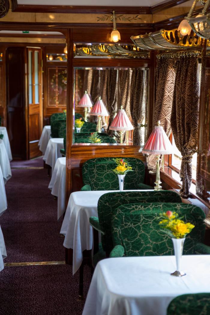 Naraţiunea trenurilor de noapte Un vagon restaurant de tren, cu fețe de masă din in, flori și lămpi umbrite
