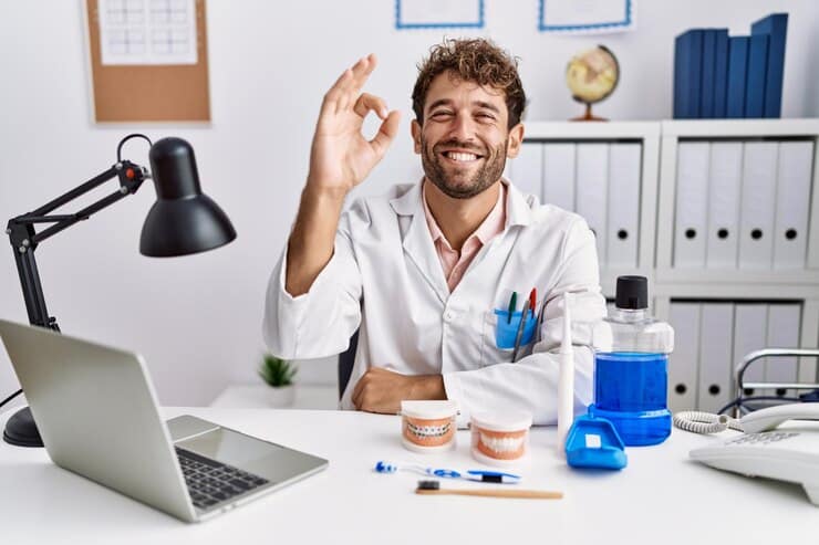 young hispanic dentist man working medical clinic smiling positive doing ok sign with hand fingers successful expression 839833 7543