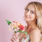 smiling blonde young woman holding flower bouquet against pink backdrop 23 2148048857