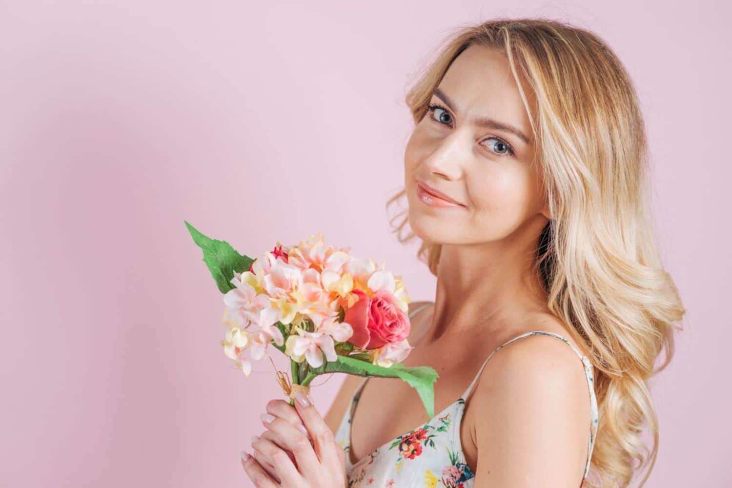 smiling blonde young woman holding flower bouquet against pink backdrop 23 2148048857