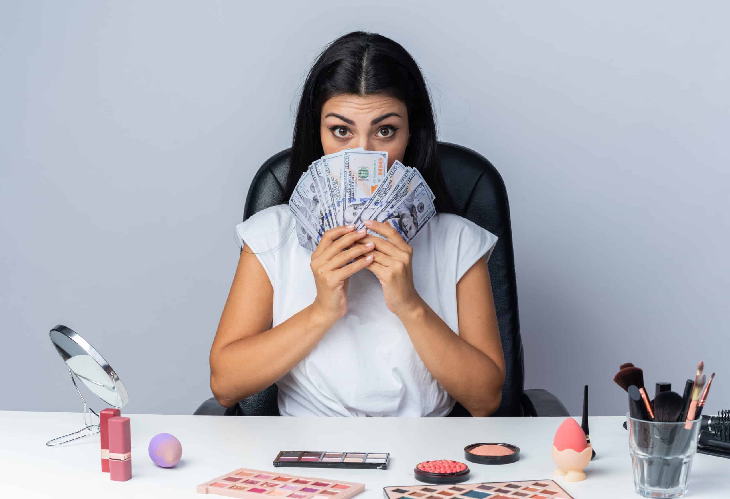 beautiful woman sits table with makeup tools covered face with cash scaled